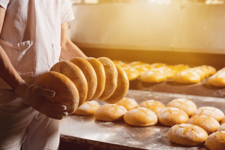 Bread in the hands of a baker on the background of an industrial oven. Industrial bread production